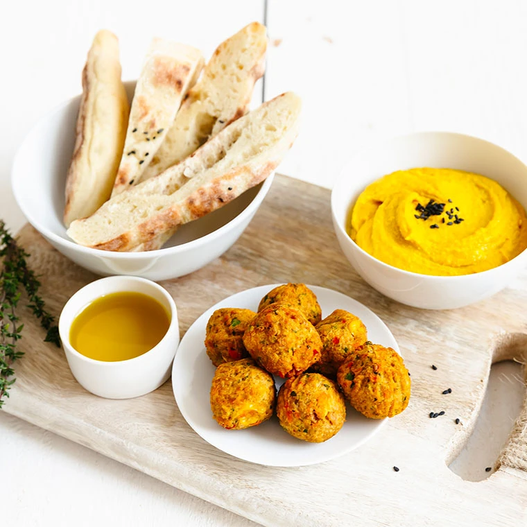 Falafel-Bällchen, Humus und Fladenbrot auf einem Holzbrett serviert.