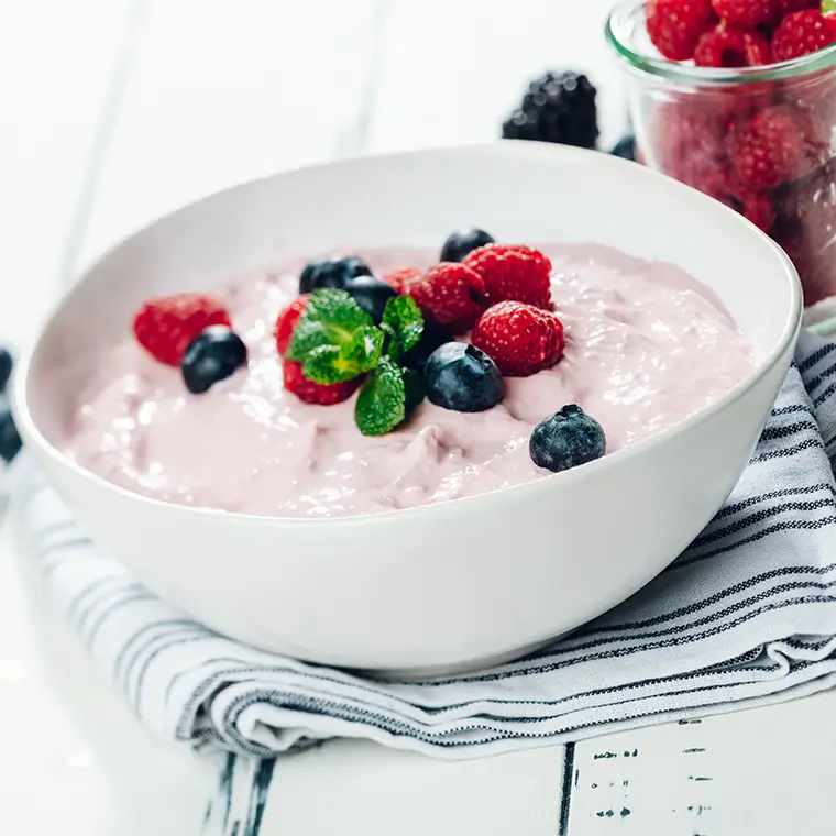 Eine Schale mit cremigem Fruchtquark, garniert mit frischen Himbeeren, Heidelbeeren und Minzblättern.