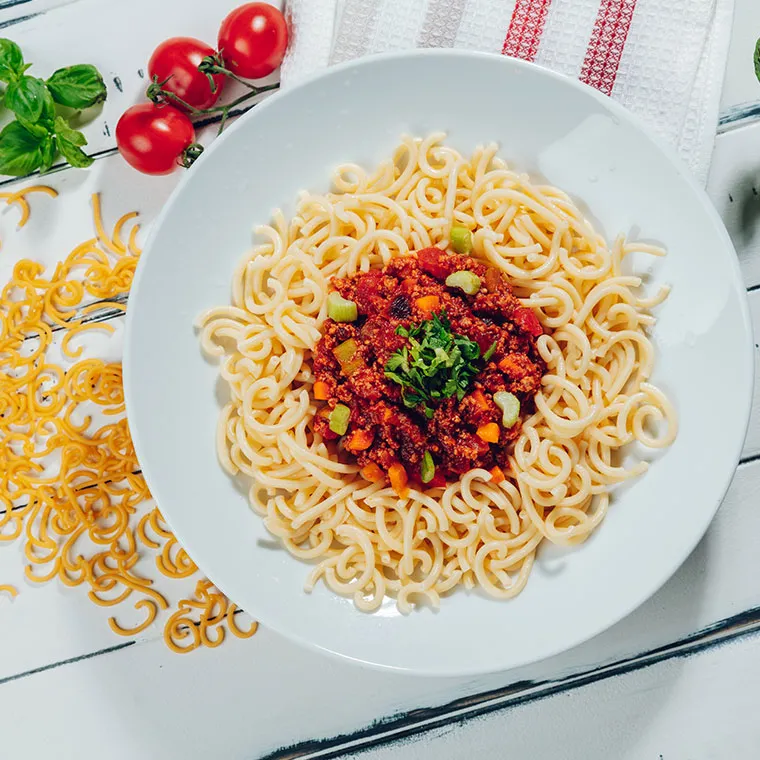Teller mit Gabelspaghetti, serviert mit einer herzhaften Bolognese-Soße und frischen Kräutern.