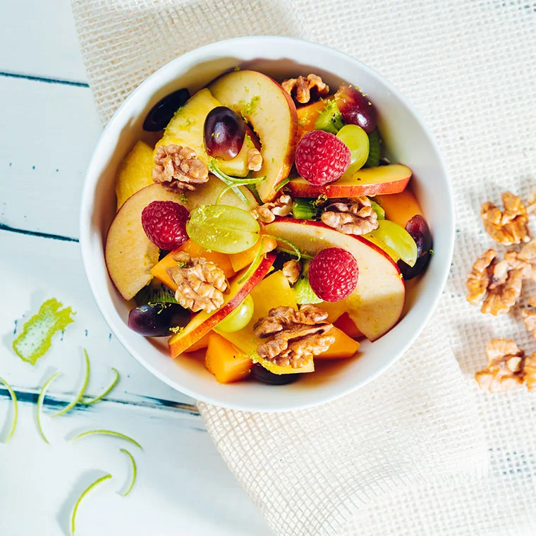 Ein Obstsalat mit Walnüssen in einer weißen Schale.