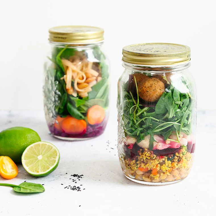 Zwei Einmachgläser gefüllt mit Salat, Quinoa, Gemüse und Falafel.