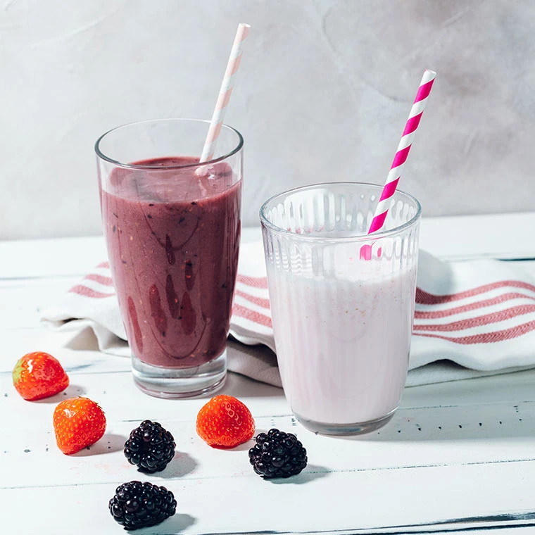 Zwei Smoothies mit Strohhalmen, umgeben von frischen Beeren.