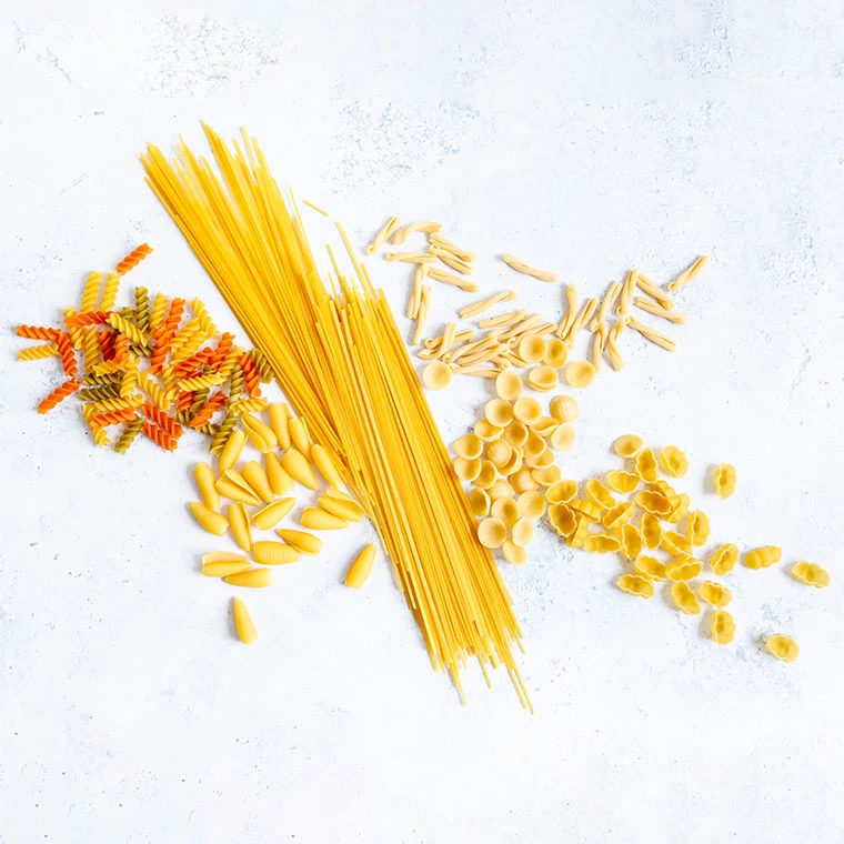 Verschiedene Nudelsorten wie Spaghetti, Fusilli, Orecchiette und Penne liegen auf einer hellen Oberfläche.