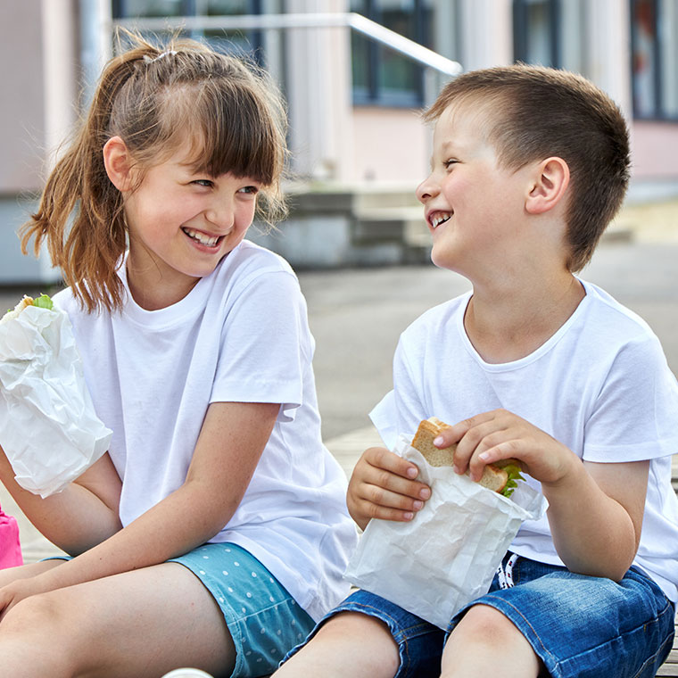 Junge und Mädchen lachen und essen in der Pause auf dem Schulhof.