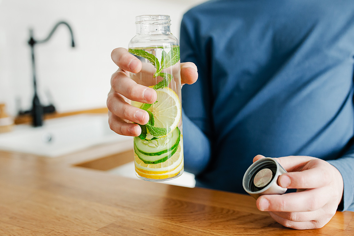 Kind hält eine Trinkflasche mit Wasser, Zitronenscheiben, Gurke und Minze.