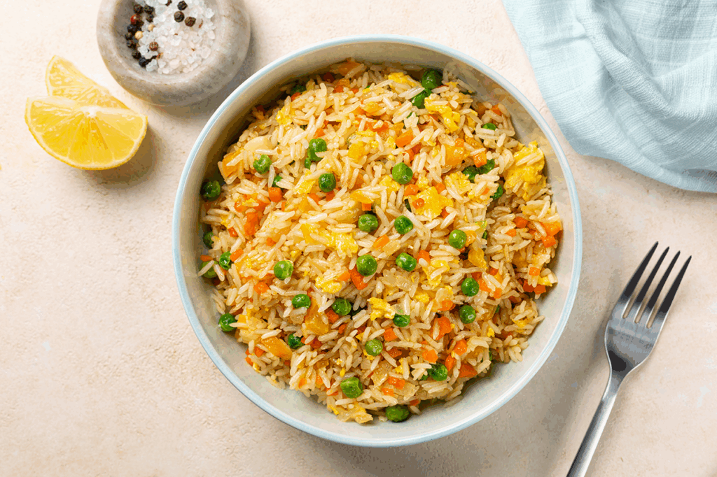 Schüssel mit bunter Reispfanne aus Reis, Erbsen, Möhren und Ei von oben fotografiert.