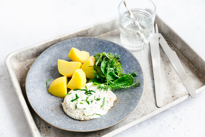Ofenkartoffeln mit Kräuterquark und frischen Kräutern auf einem grauen Teller serviert.